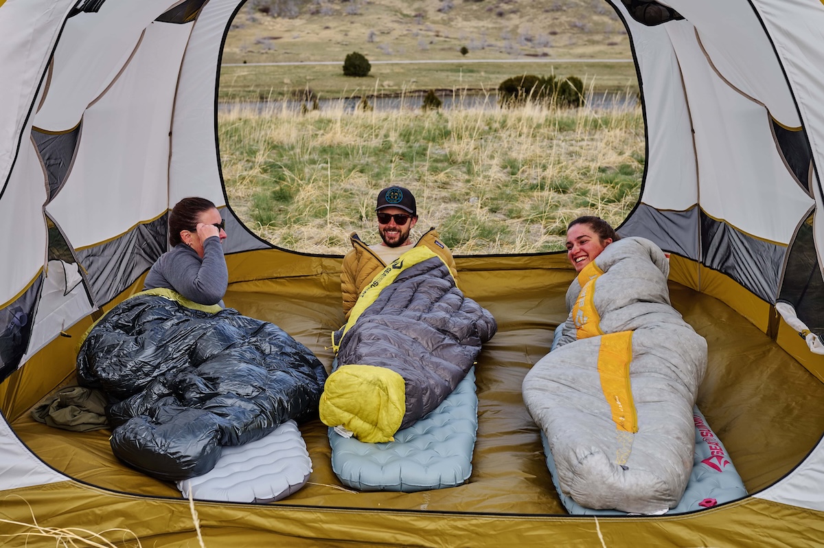 Three friend hanging out in a tent in their sleeping bags, smiling and laughing