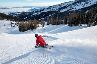 A man skis downhill at a ski resort in the mountains.